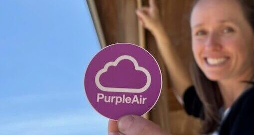 Brittany Keyes holds up a PurpleAir sensor logo while mounting a sensor