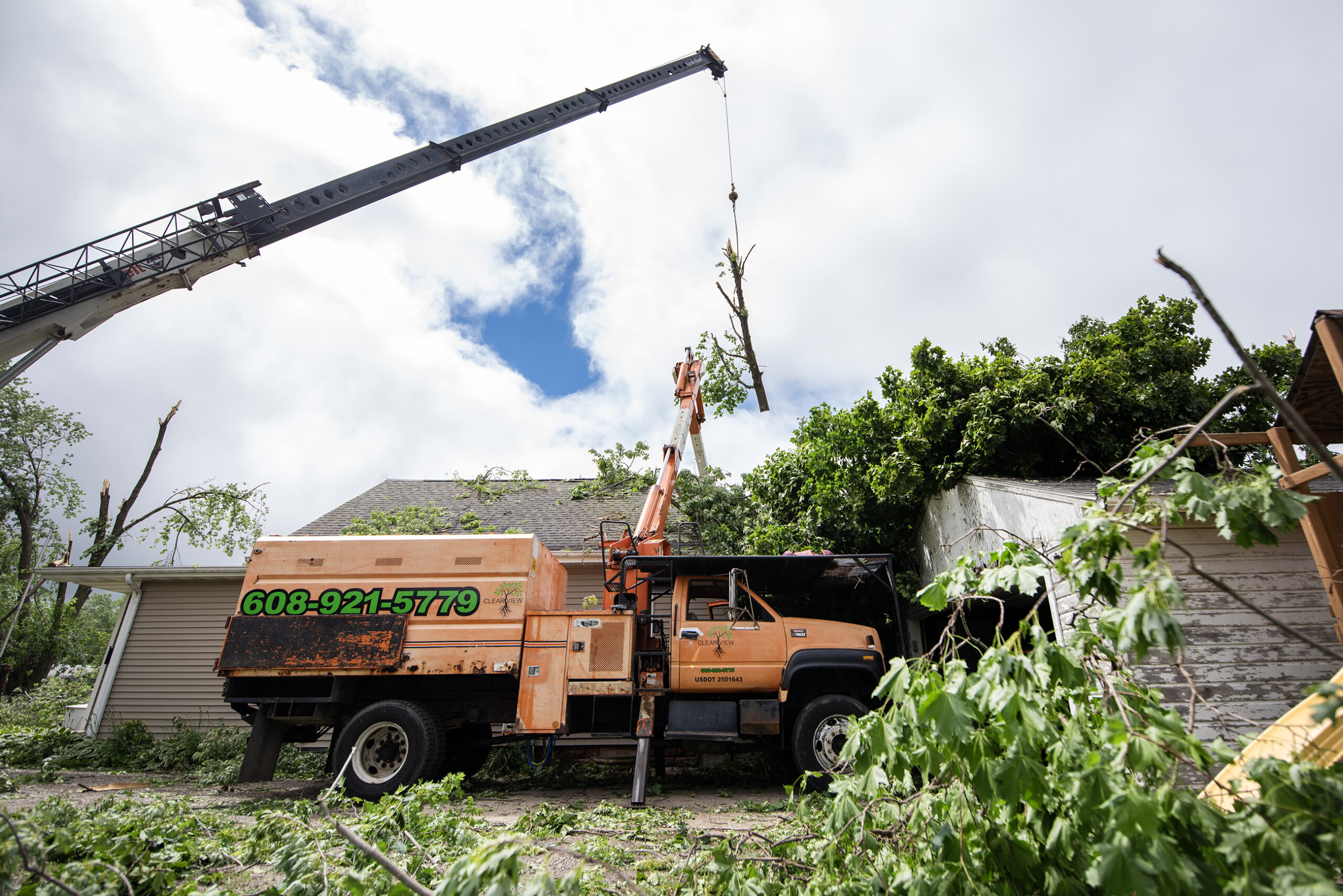 A crane pulls a large part of a tree off of a house.