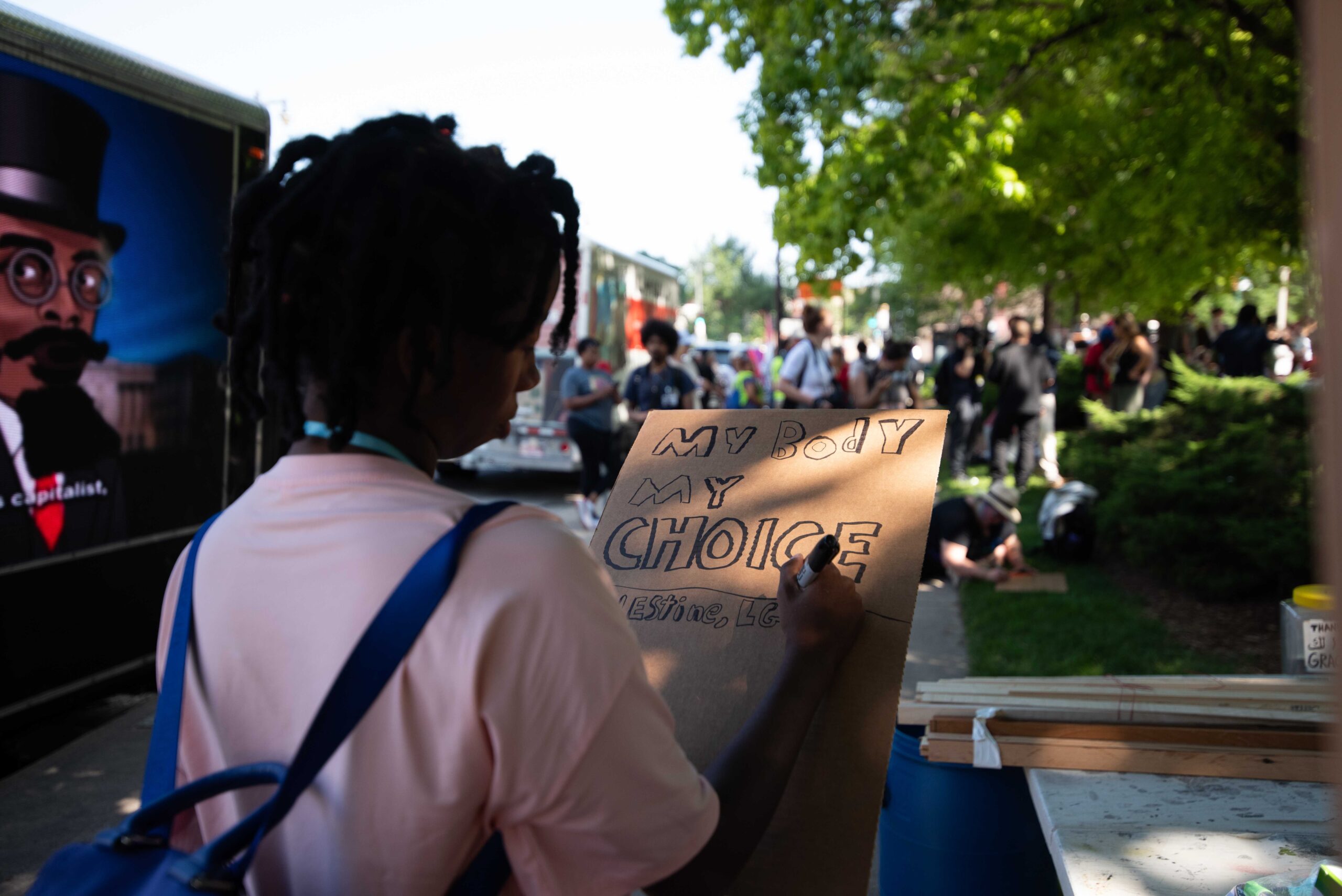 Asayca Noblin, from Milwaukee, writes on a sign as protesters to the Republican National Convention congregate in Red Arrow Park in Milwaukee. This is the first protest for Noblin, who said she cares about LGBTQ issues and Palestine. "I don't want Trump here," she said. Angela Major/WPR