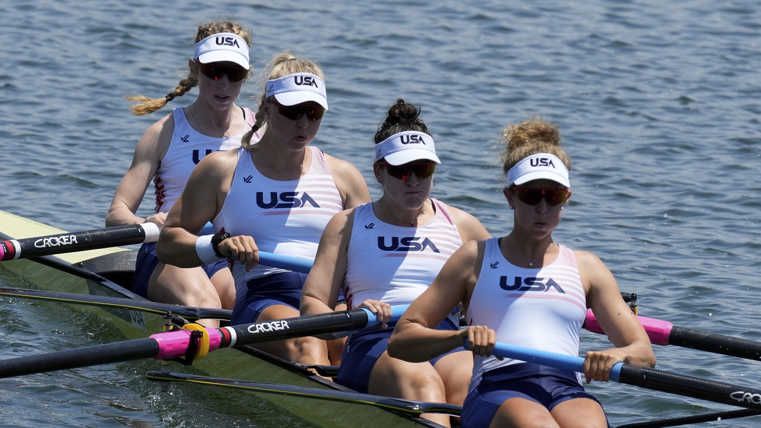 For women row together in a slim rowing boat. They're wearing matching uniforms that read "USA."