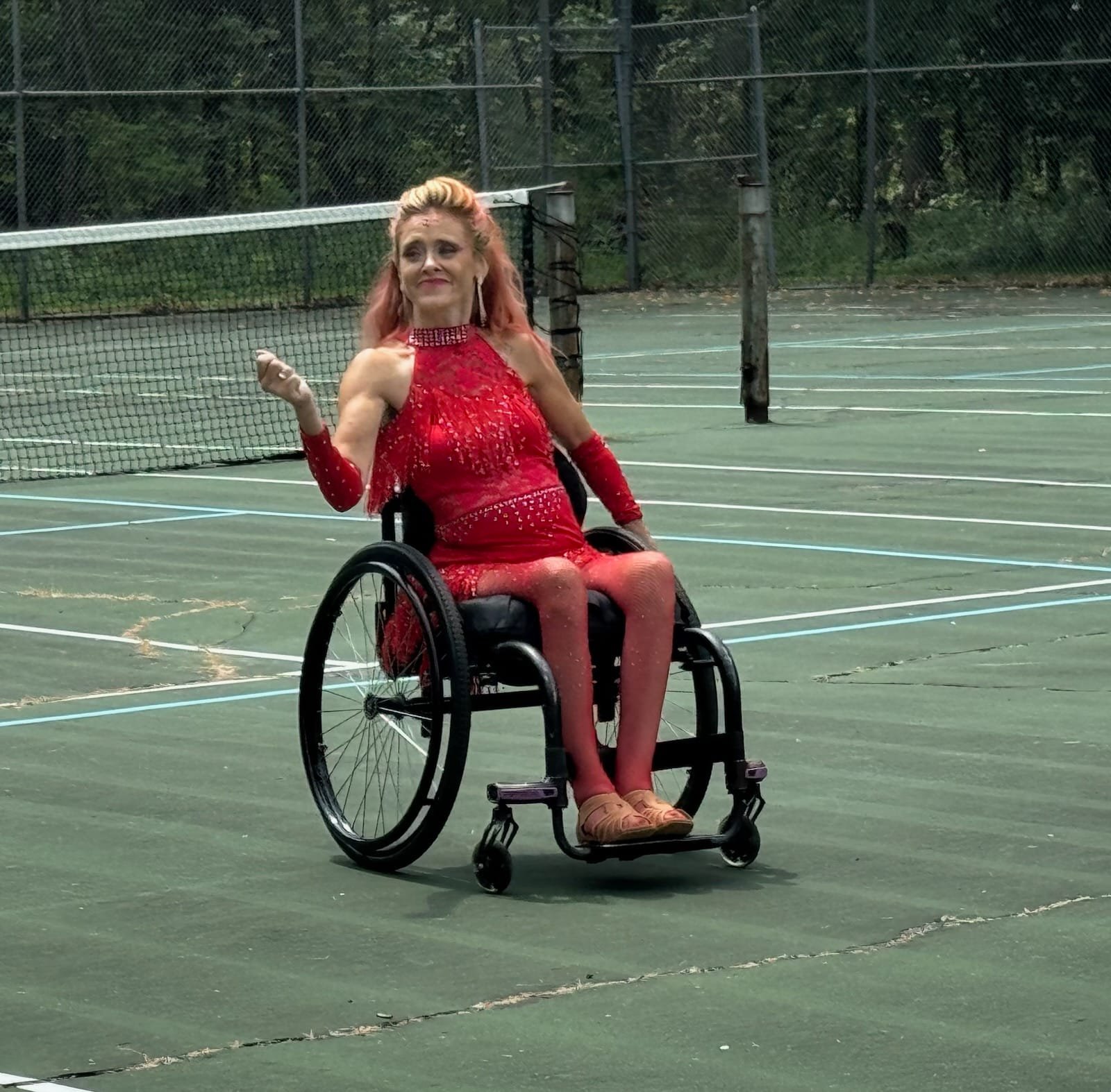 A woman in a sparkly red dress sits in a wheelchair on a tennis court