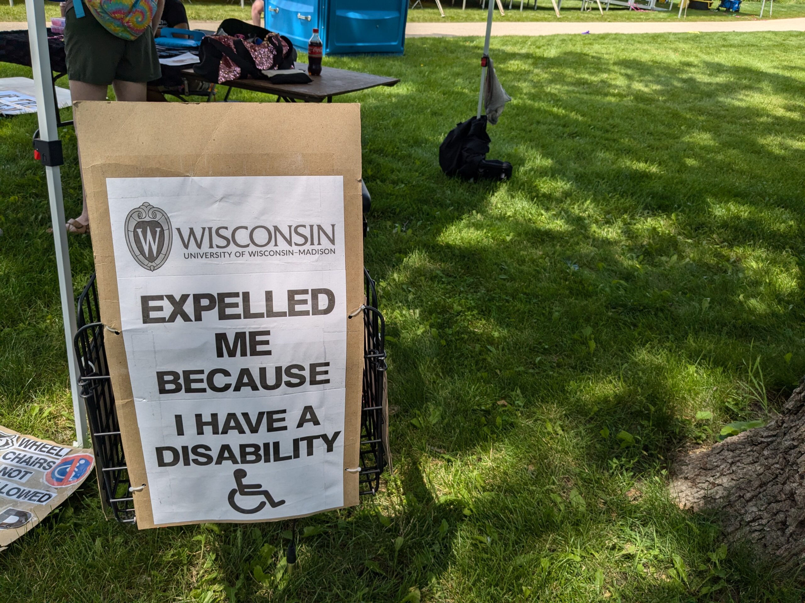A sign reading "University of Wisconsin-Madison expelled me because I have a disability" with a wheelchair icon at the bottom