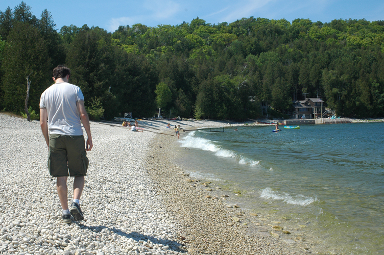 A man walks along a beach filled with pebbles with the lake on his right