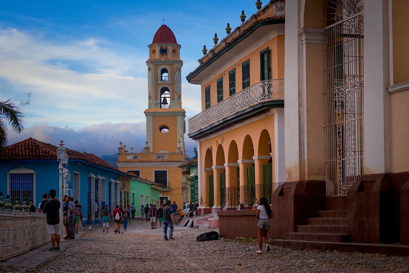 A street on the Caribbean island of Trinidad features a church and other colonail architecture. A woman is walking down the street.