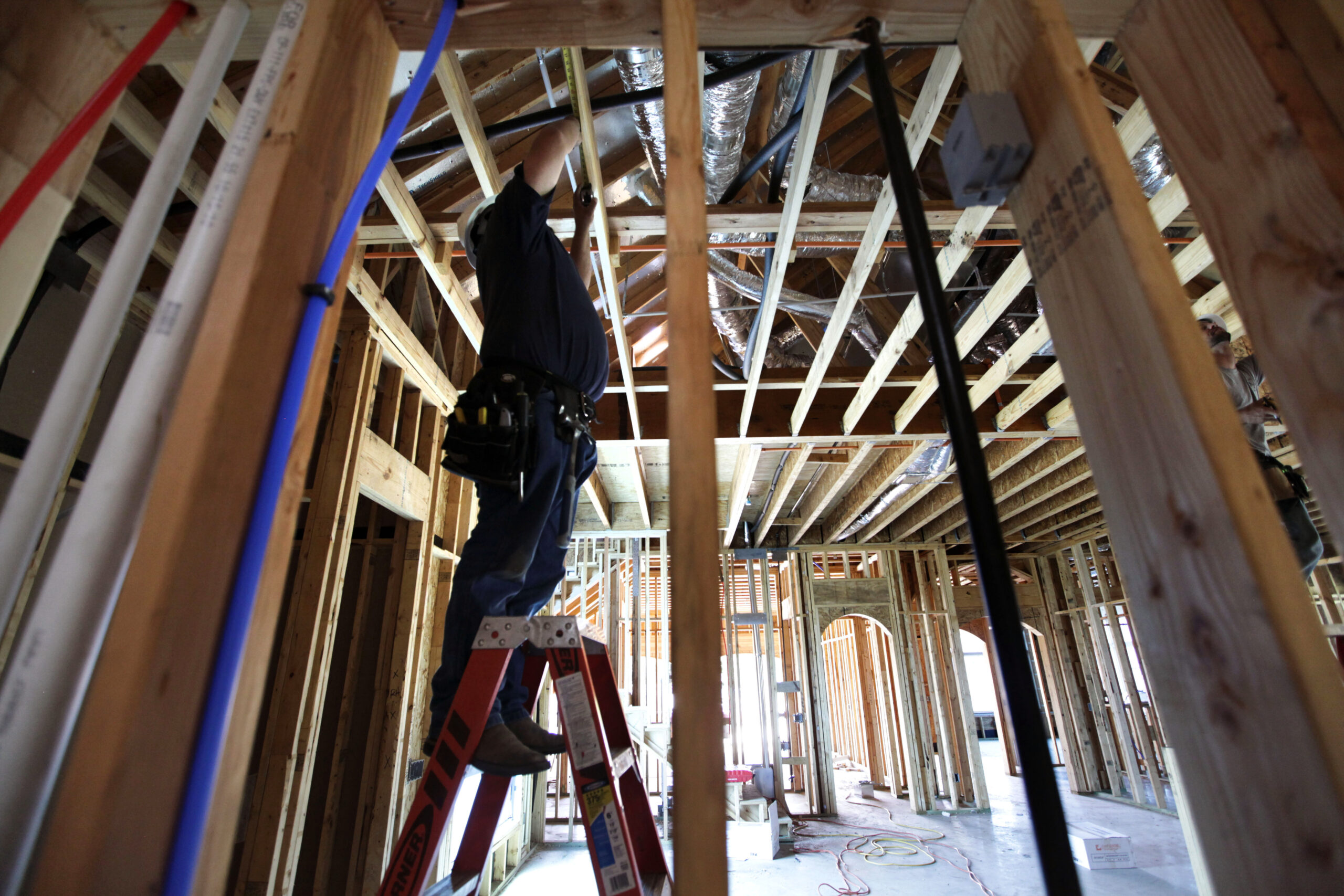 A man stands on a ladder and attaches wires to a home under construction.