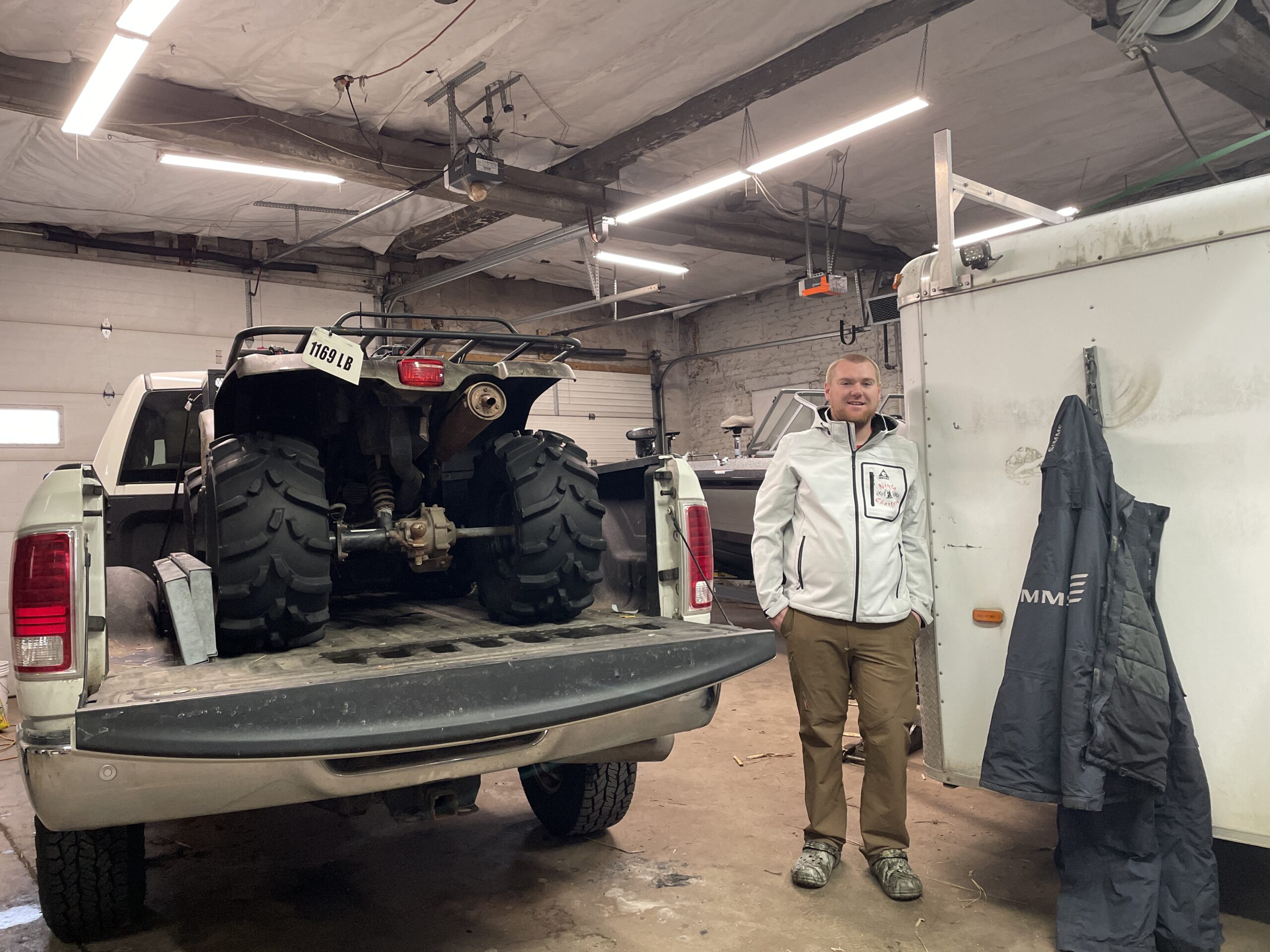 Luke Chatfield, who runs the Ninja Fishing charter, WI, stands with his truck, ATV, and boat in his Port Washington garage on Dec. 17, 2024.