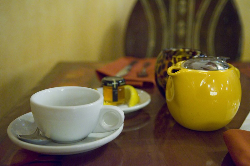 A tea cup in a saucer and a small tea pot sit on a table. 