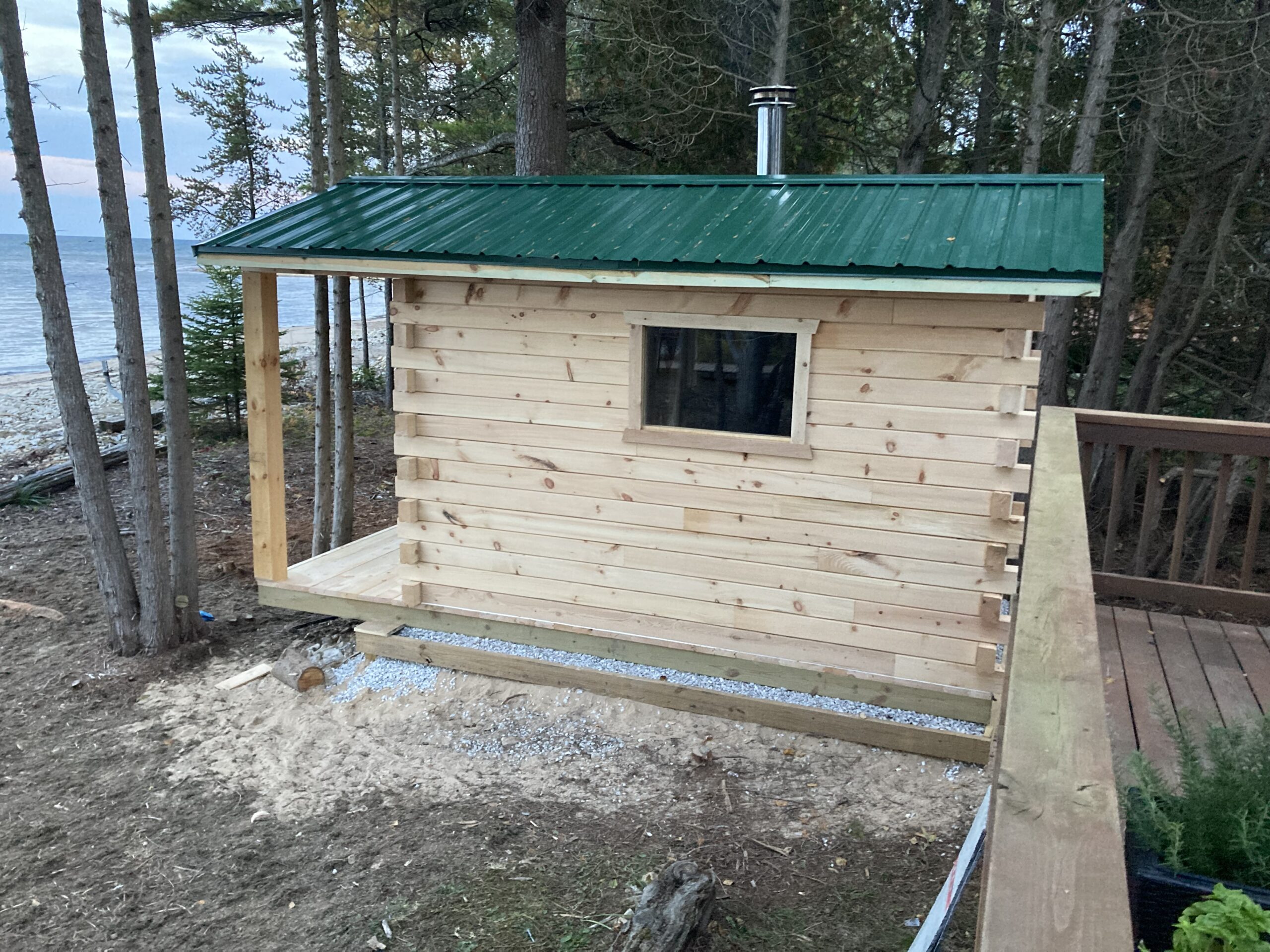 A sauna with wood siding and a tin roof sits at the edge of a lake.