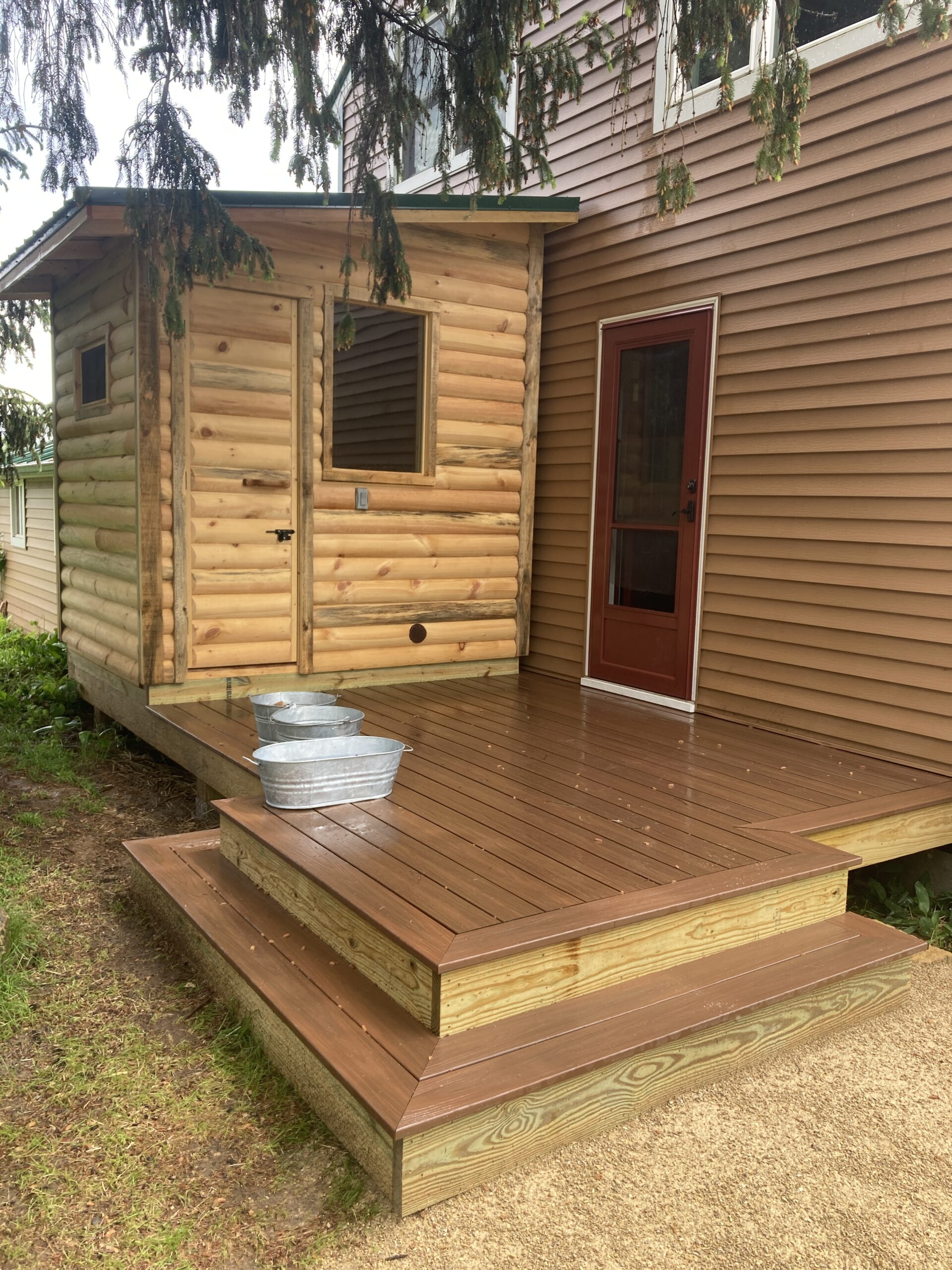 The exterior of a wooden sauna that's been built right outside of a house, on a back porch. 