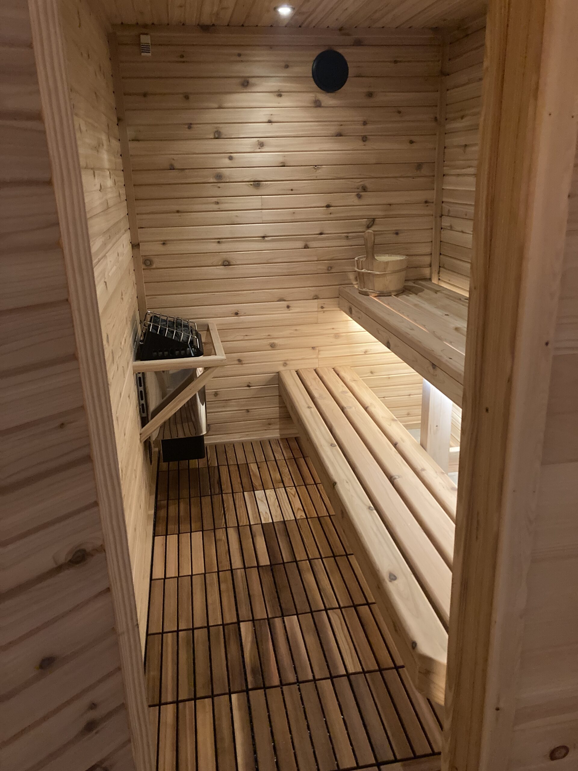 The interior of a wooden sauna. There's a bench, heater and small bucket. 