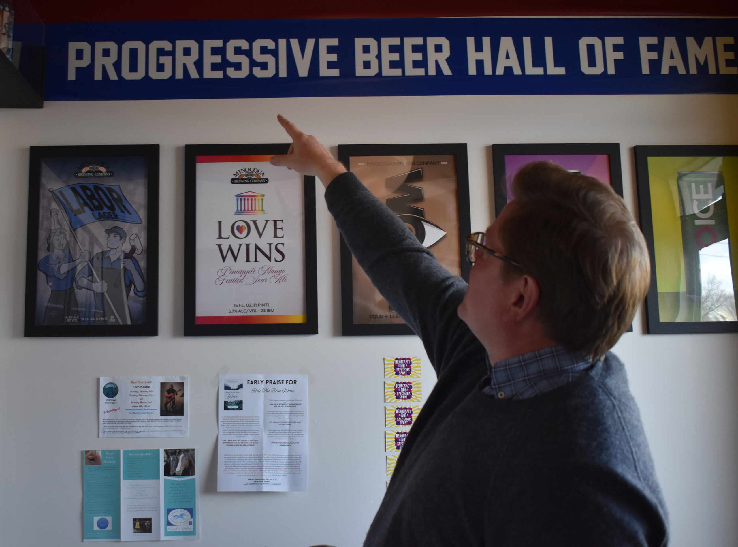 Kirk Bangstad points out the "Progressive Beer Hall of Fame" at the Minocqua Brewing Company Madison Taproom. <em>Rob Mentzer/WPR</em>