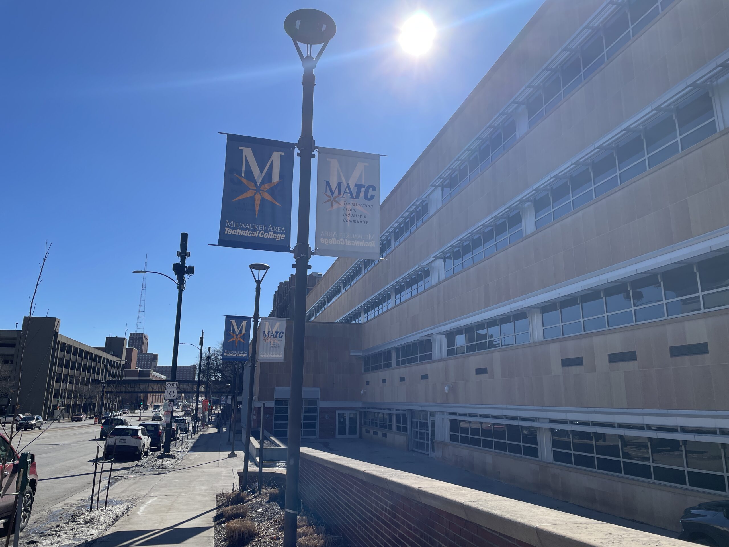 Street view of a college building under a clear sky, with banners displaying the logos of Milwaukee Area Technical College on the light poles.