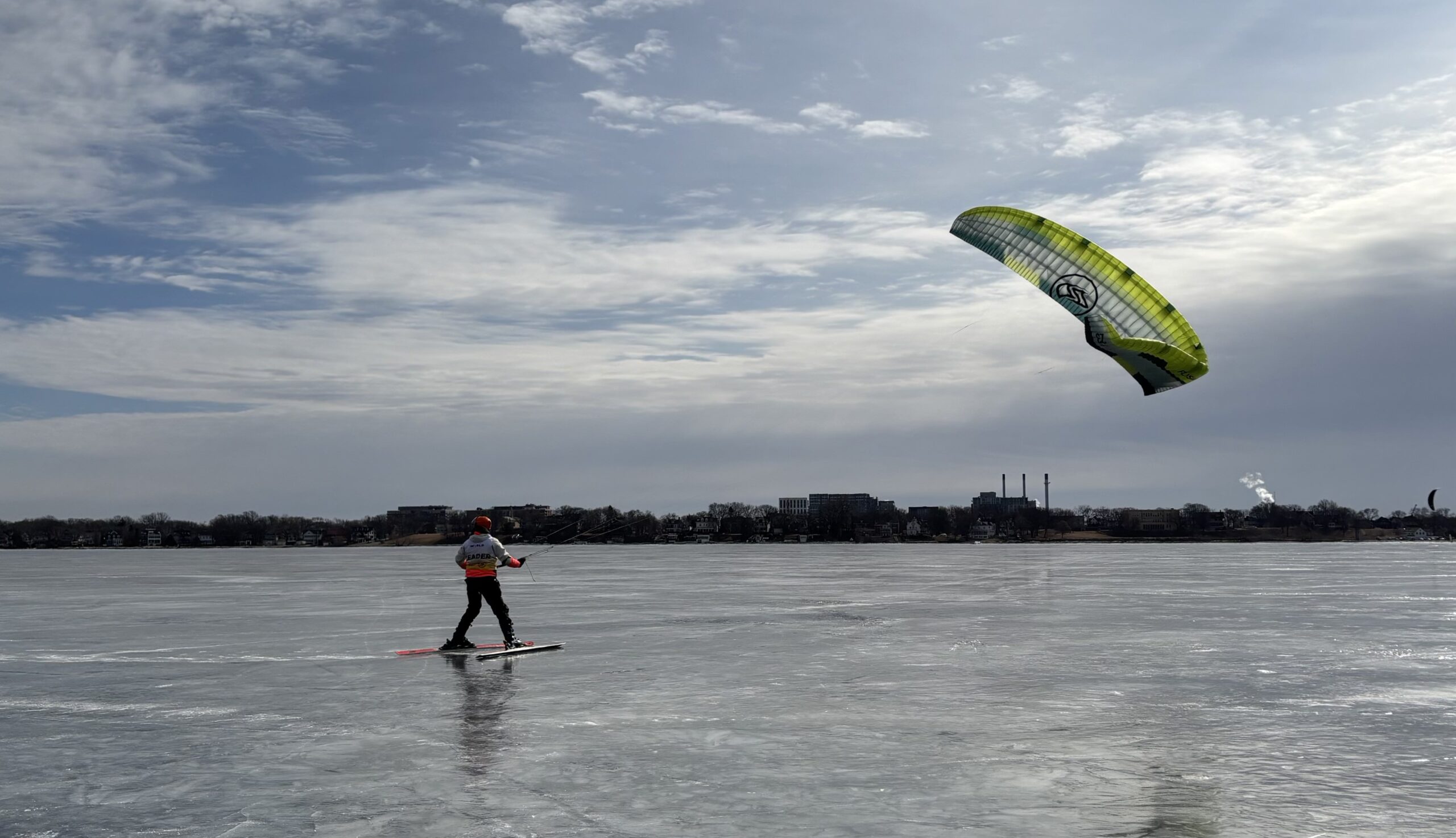 Person kite skiing on a frozen lake with a partly cloudy sky.