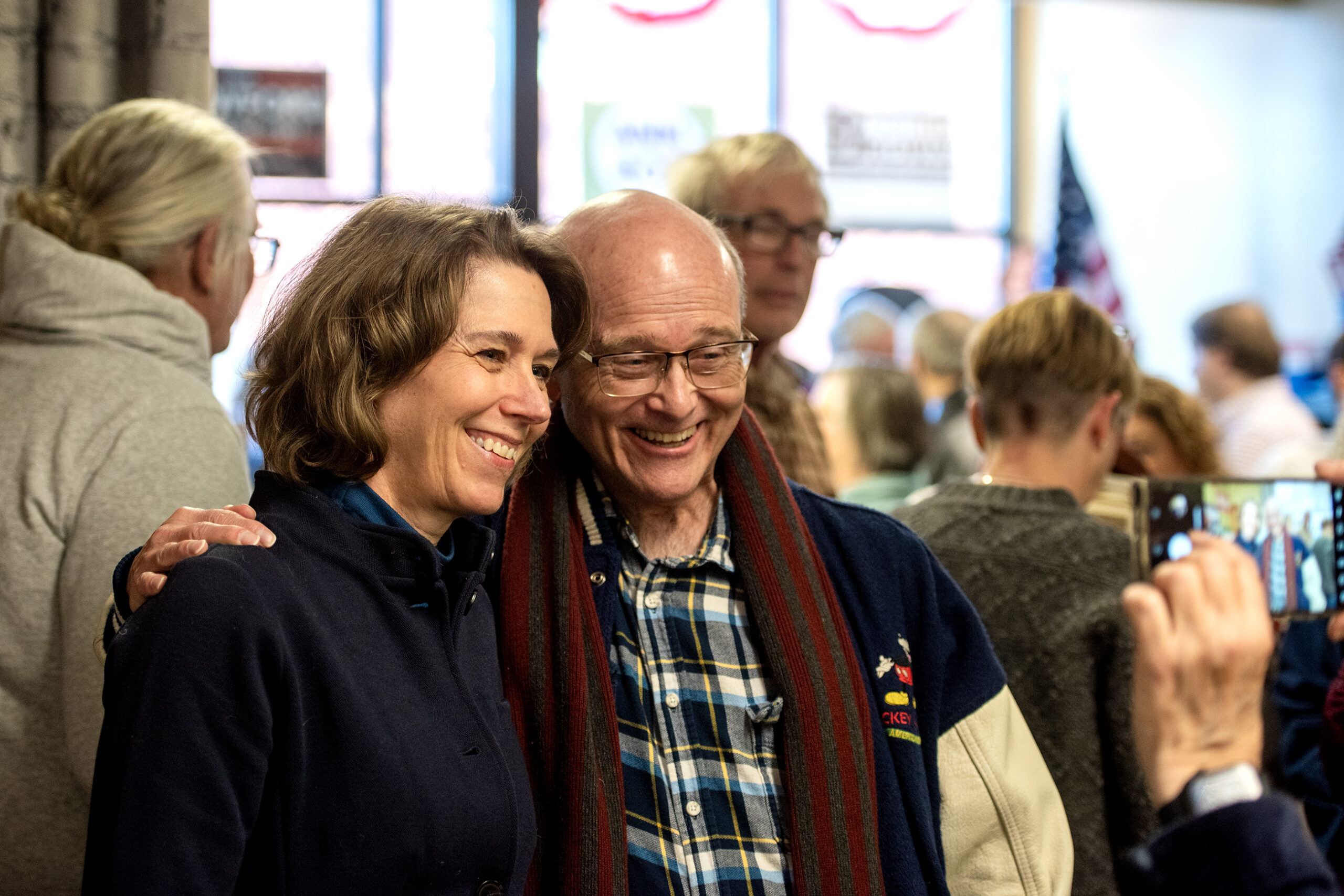 A woman and an older man stand together smiling as a group of people engage in conversation around them.