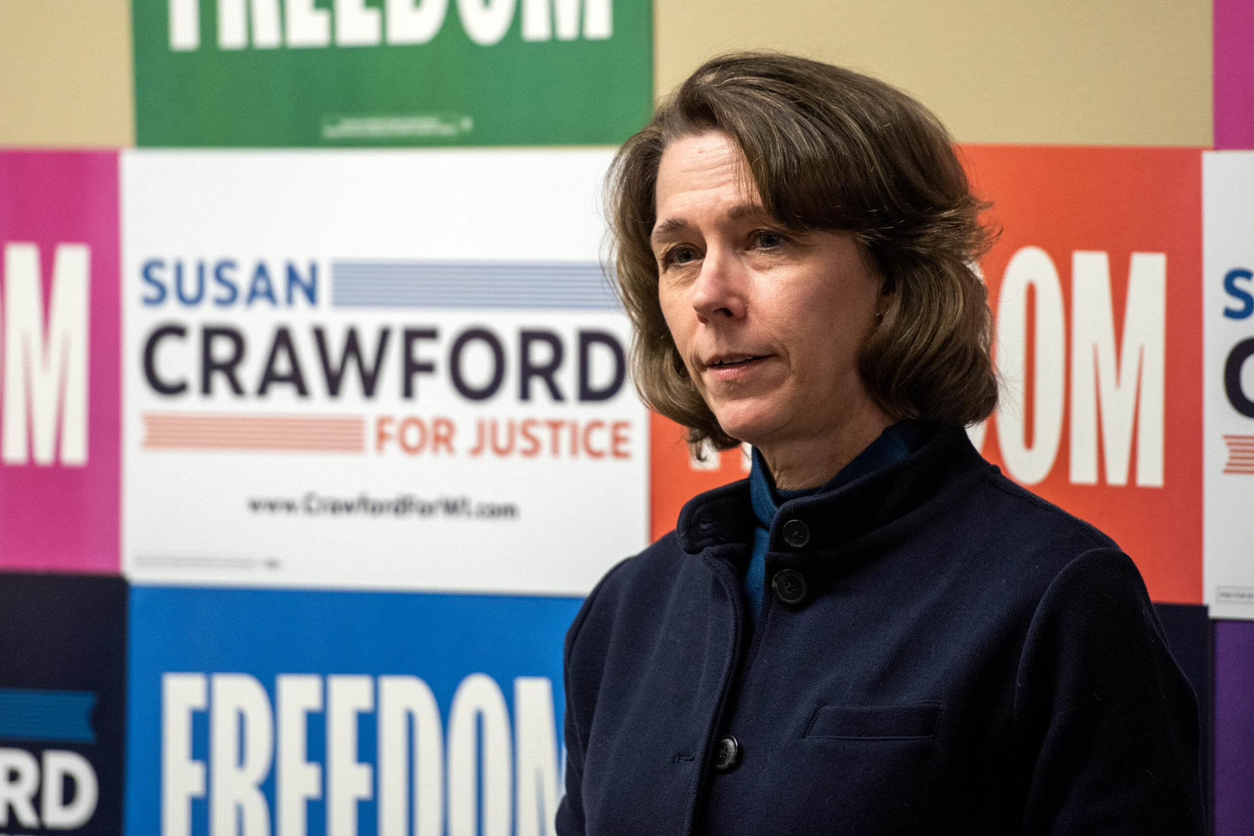 A woman stands in front of colorful campaign posters with the words Freedom and Susan Crawford for Justice visible.