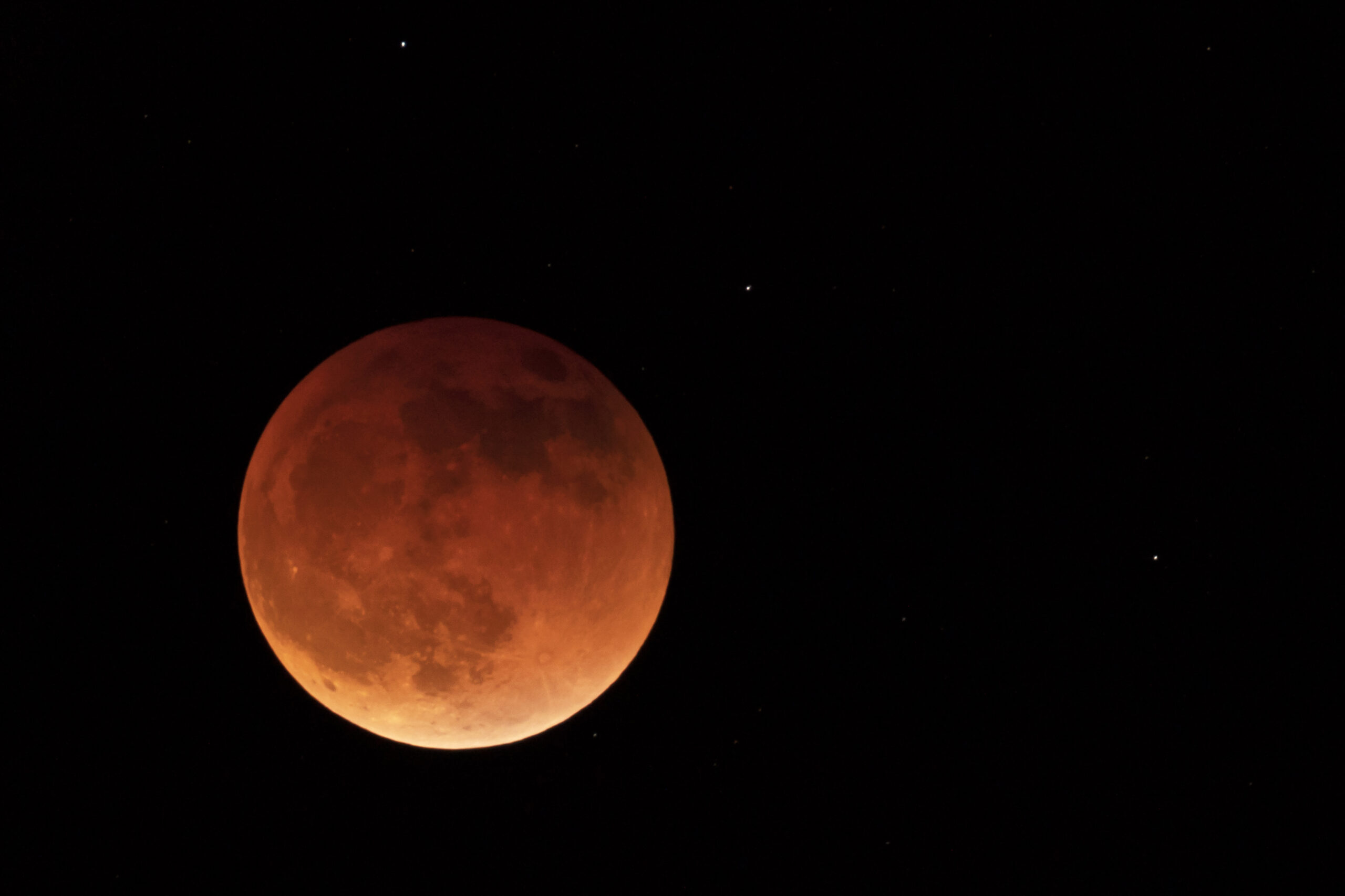 A red-hued lunar eclipse against a dark night sky with scattered stars visible.