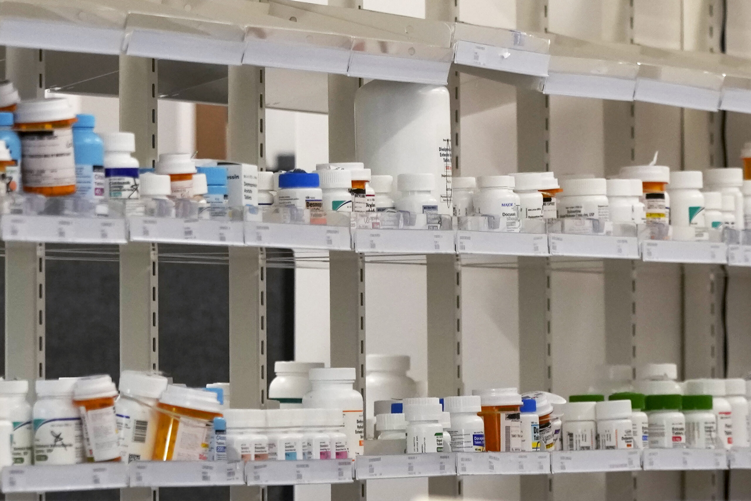 Shelves filled with various prescription medication bottles, organized in rows at a pharmacy or medical facility.