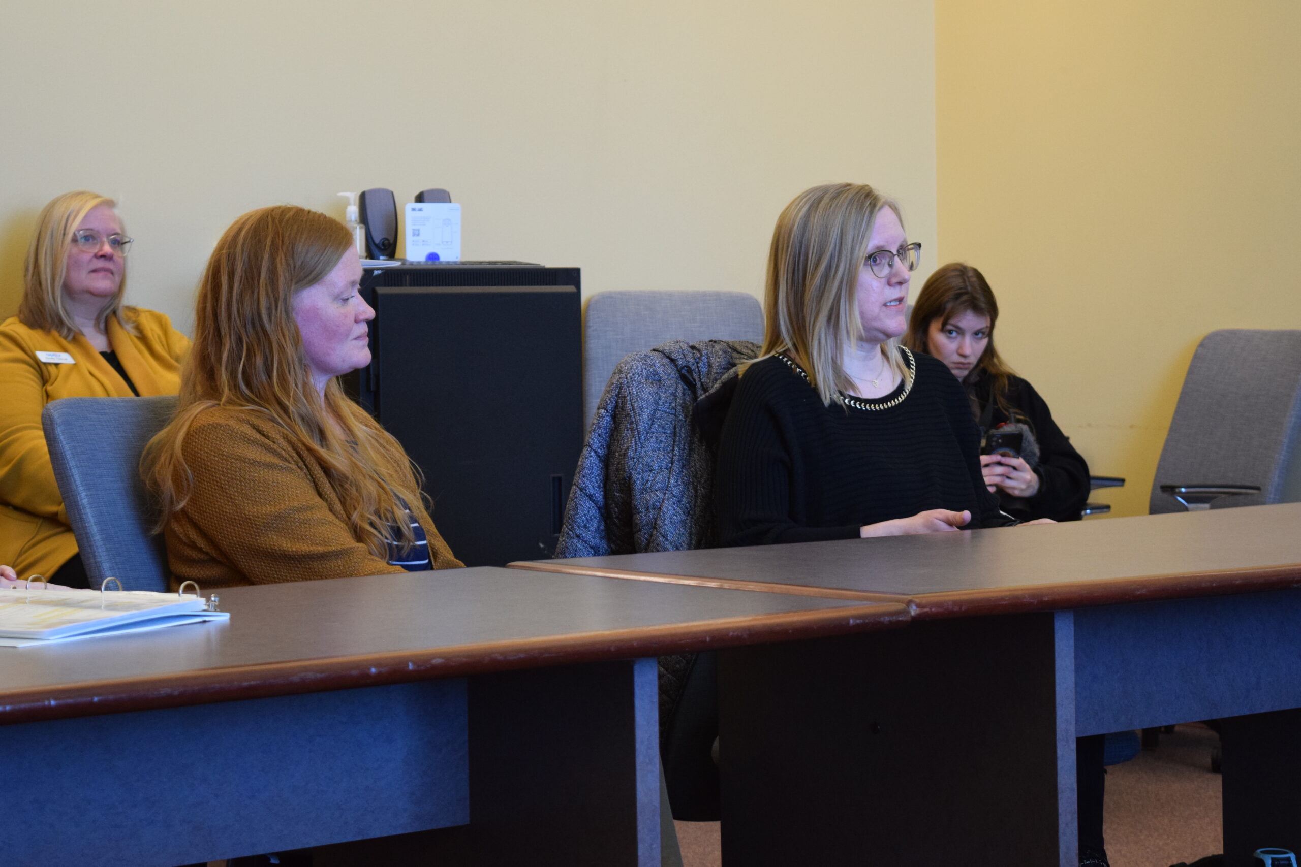 People seated in a meeting room, listening attentively with a presentation on the screen.