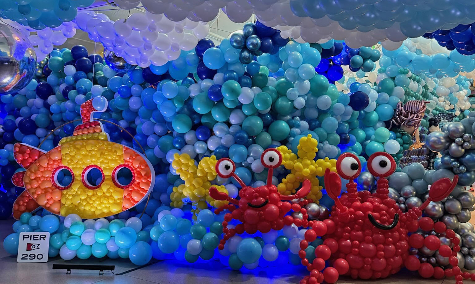 Colorful balloon display featuring a yellow submarine, red crabs, and blue sea-themed designs with a Pier 290 sign on a stand.