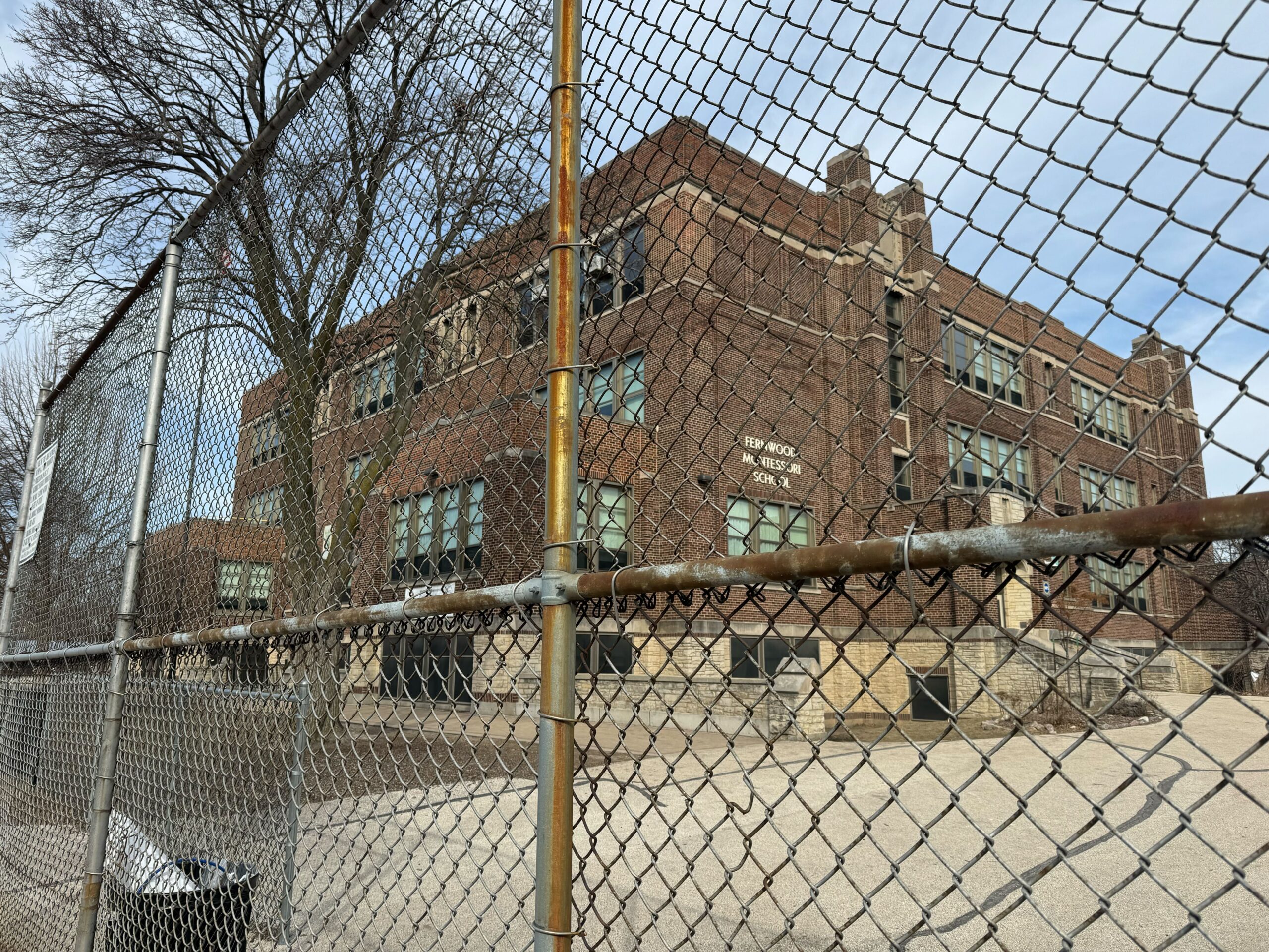 A large, old brick building is behind a chain-link fence. Leafless trees are visible, and the sky is cloudy. The sign on the building reads JEFF MEDIA.