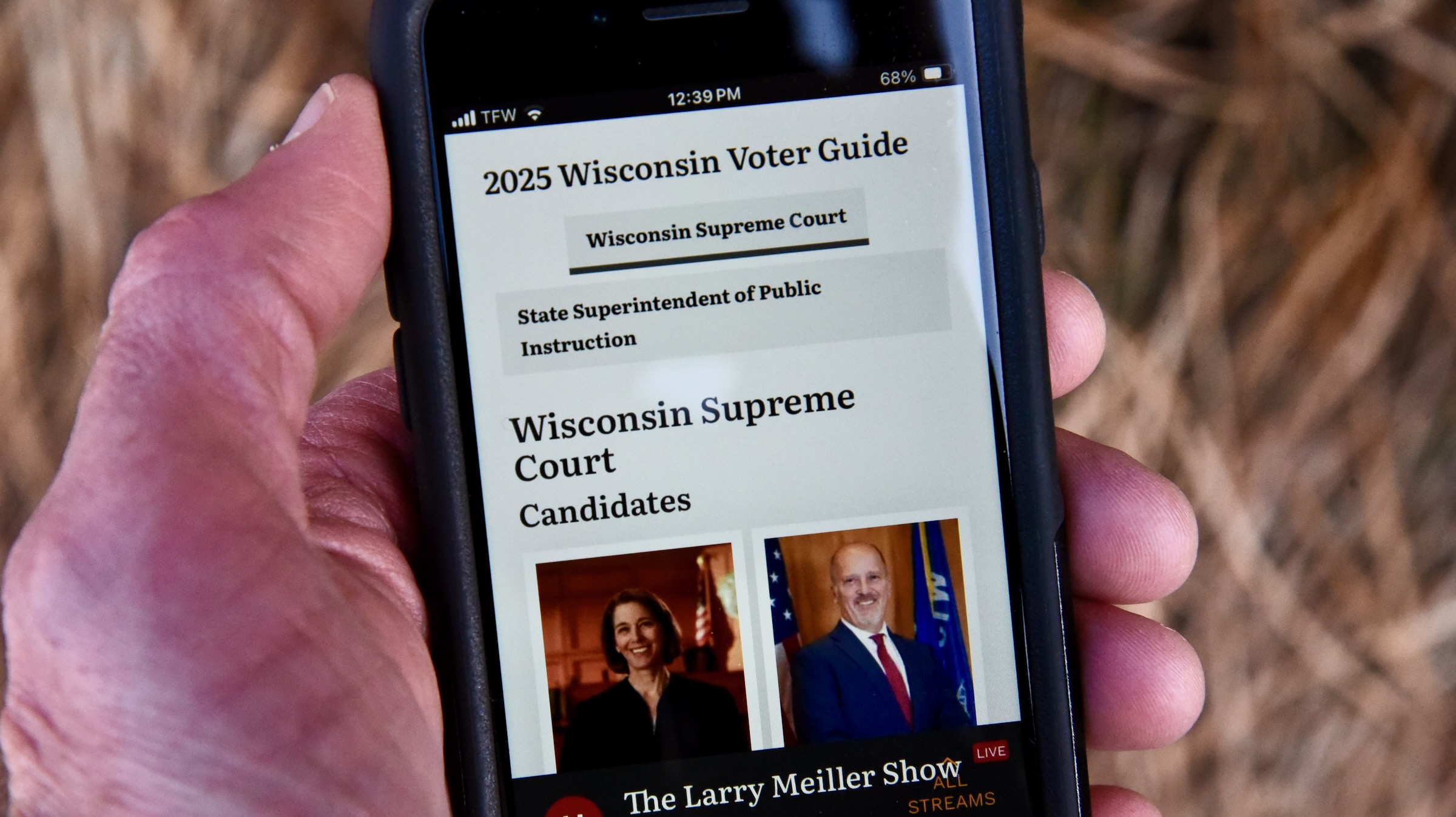 Hand holding a smartphone displaying a 2025 Wisconsin Voter Guide with information on Supreme Court candidates.