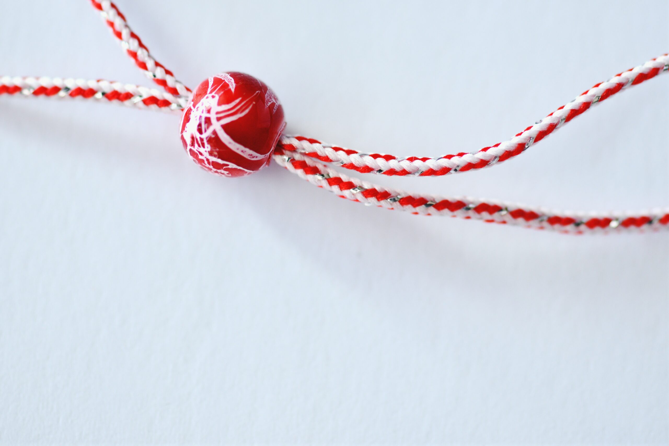 Close-up of a red and white braided string with a red bead in the center, set against a plain white background.