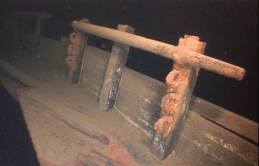 Underwater view of a sunken shipwreck with rusted metal parts and encrusted coral or marine growth on wooden structures.