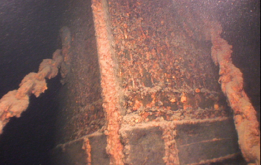 Underwater view of a rusted shipwreck with corroded metal surfaces and marine growth attached to its structure.